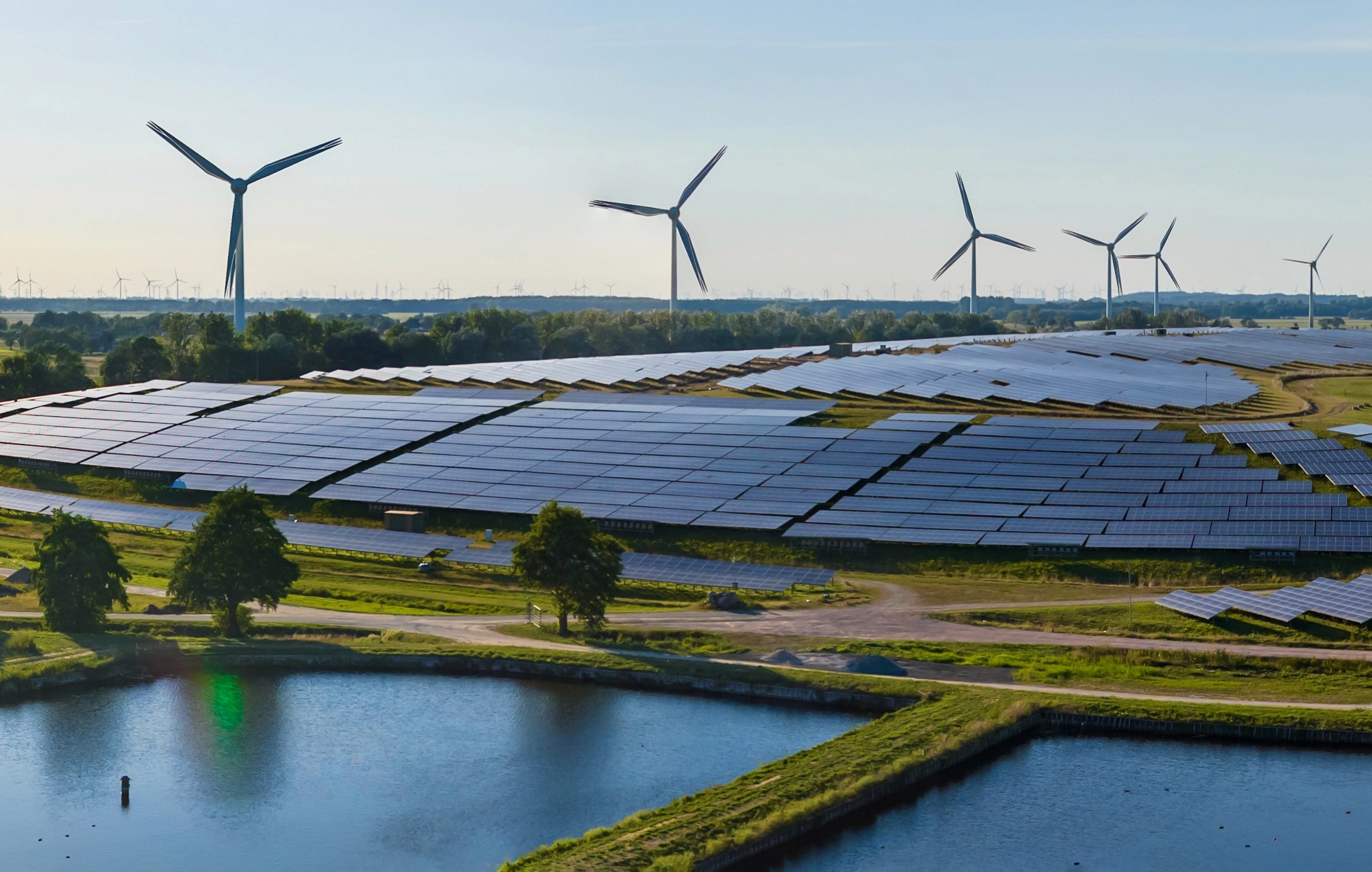 A picture of a solar farm with wind turbines in the background